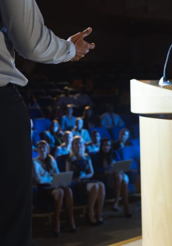 Rear view of businessman giving presentation in front of audience in auditorium